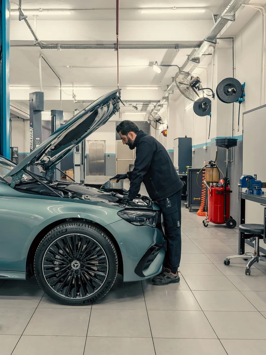 Technician leaning into the engine bay of a grey sedan in a bright workshop